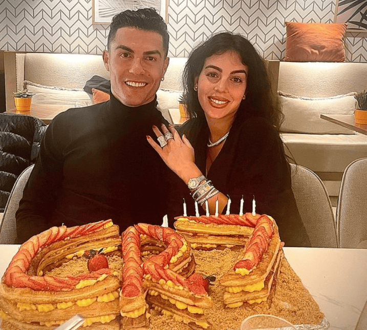 Cristiano Ronaldo and girlfriend Georgina Rodriguez sharing a joyful birthday celebration, seated before a beautifully adorned birthday cake.