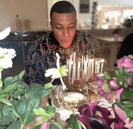 Kylian Mbappe, beaming blows out a birthday candle, capturing a solitary yet joyful moment of celebration.