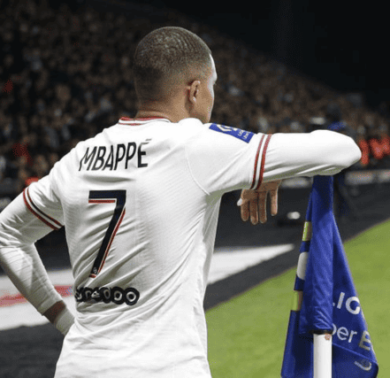 Kylian Mbappe, donning the iconic number 7 jersey, confidently holds the corner flag, a symbol of his prowess and leadership on the pitch.